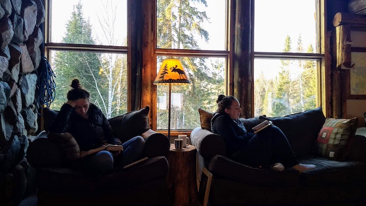 two women read in comfortable chairs in a rustic lodge